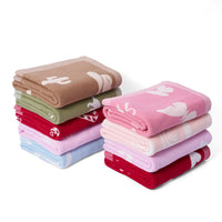 Stacks of neatly folded multi-colored baby blankets including cacti, olive green, red candy cane, blue, and pink designs