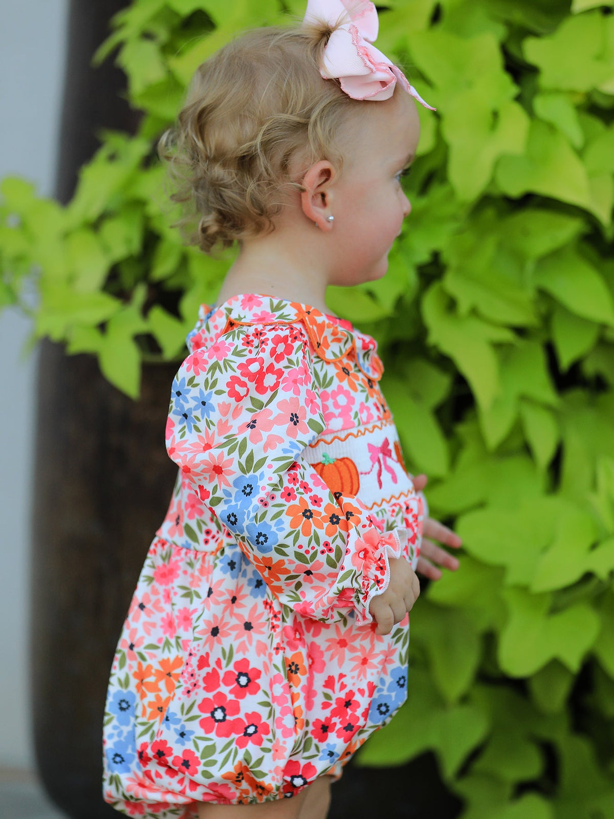 Fall Halloween Pumpkin Bow Smock Romper with floral embroidery; cute baby girl with pink bow headband outdoors.