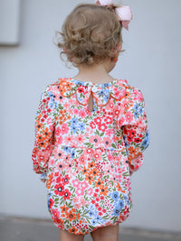 Back view of a floral baby girl romper with scalloped orange trim and a white button, plus pink hair bow.