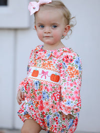 Toddler girl wearing a fall floral pumpkin-embroidered smock romper with a pink bow headband.