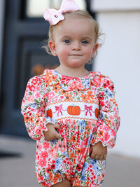 Baby girl in a floral Fall pumpkin bow smock romper with pumpkin embroidery and pink headband.