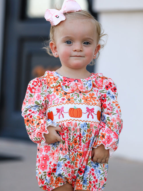 Baby girl in a floral Fall pumpkin bow smock romper with pumpkin embroidery and pink headband.