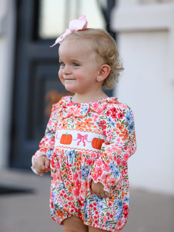 Baby girl in a floral pumpkin-embroidered smock romper with a pink bow headband.