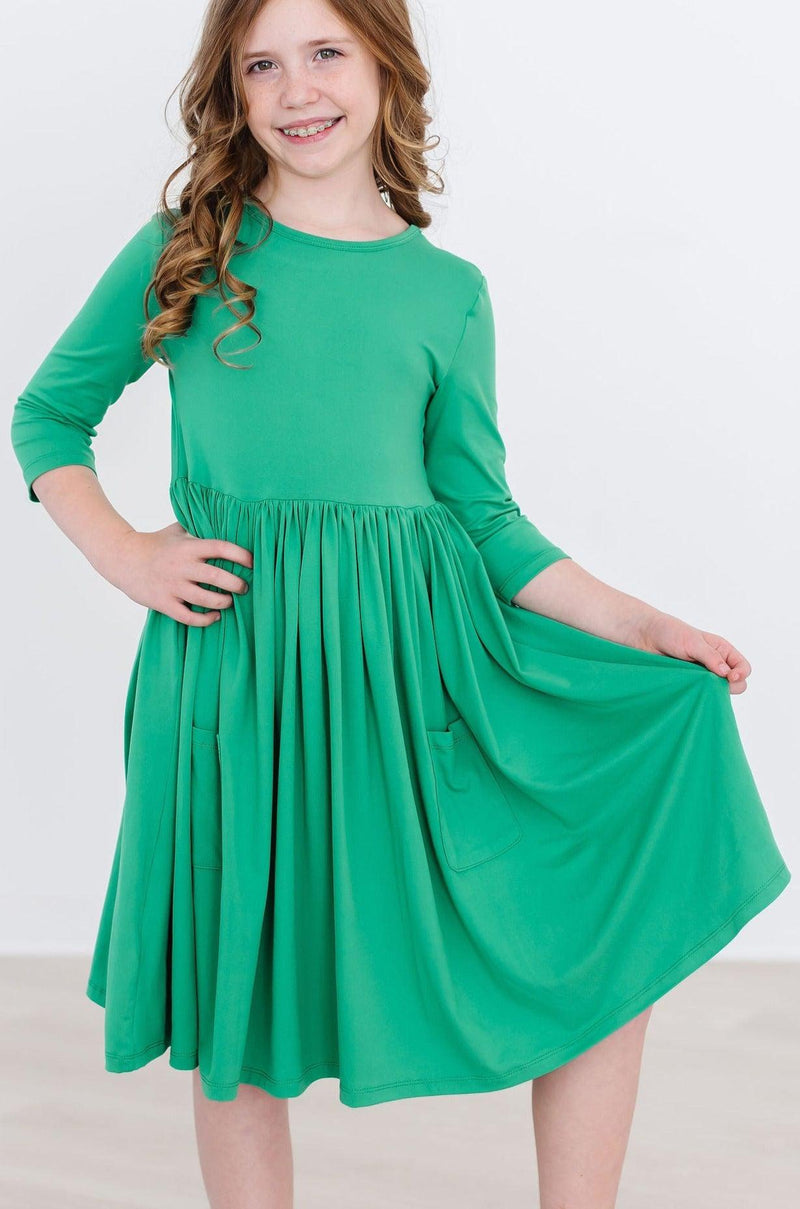 A young girl joyfully twirling in a Kelly Green 3/4 Sleeve Pocket Twirl Dress by Mila & Rose, showcasing the dress's vibrant color and playful design.