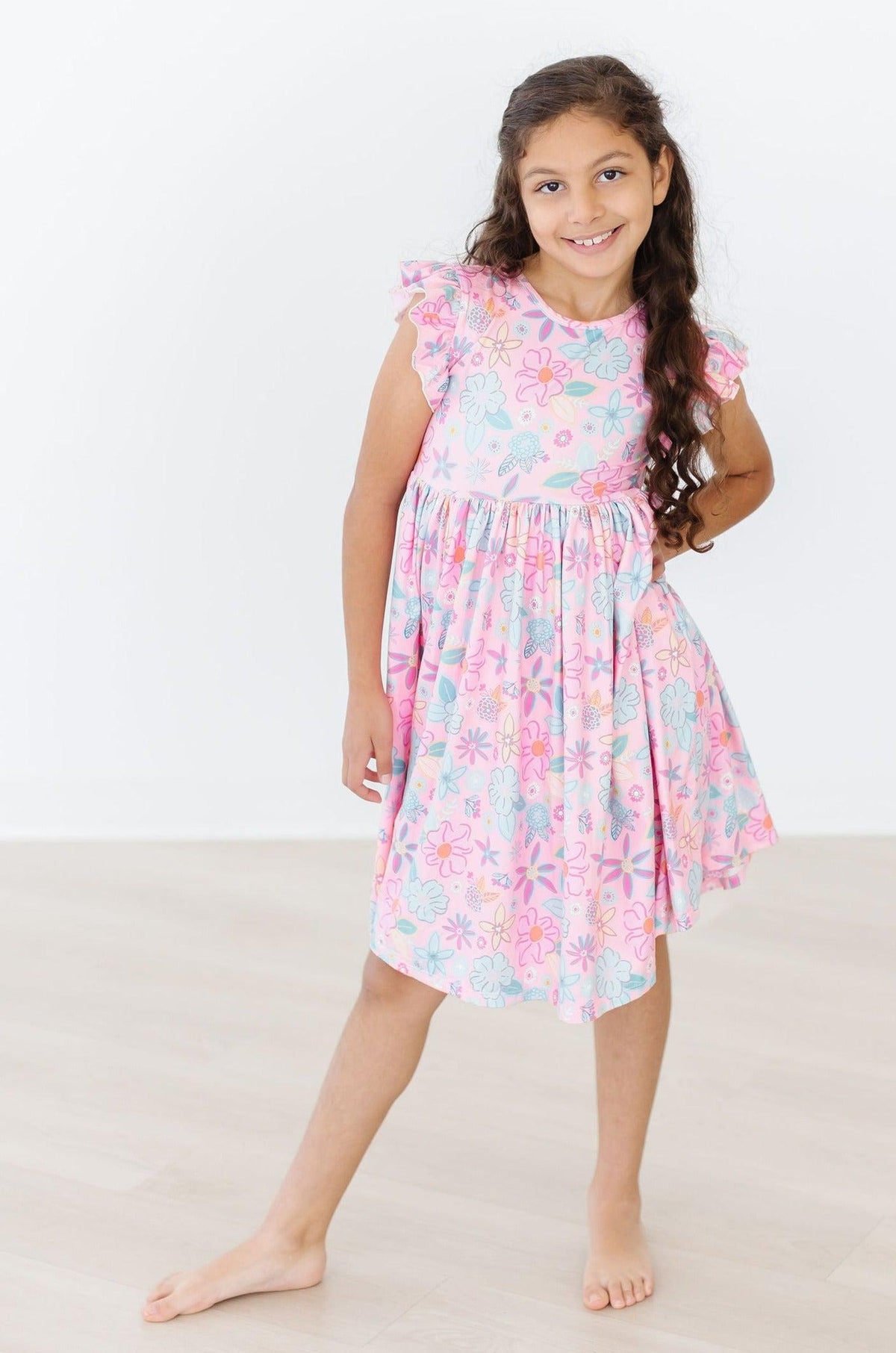 Girl wearing a pink floral flutter sleeve twirl dress with comfortable ruffle details for play.