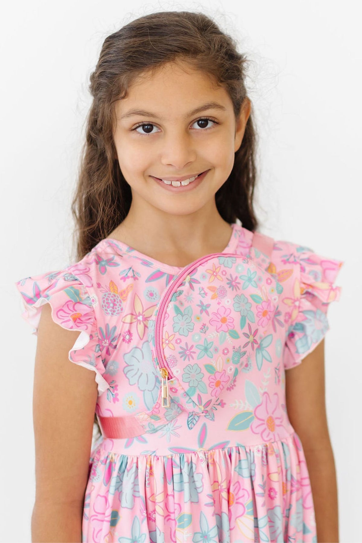 Girl wearing pink floral Flutter Sleeve Twirl Dress with ruffled cap sleeves and front zipper detail.