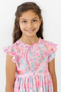 Girl wearing pink floral Flutter Sleeve Twirl Dress with ruffled cap sleeves and front zipper detail.