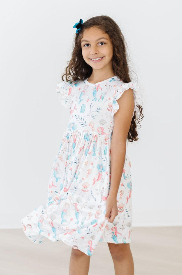 Mermaid Friends Flutter Sleeve Twirl Dress on a smiling girl with pastel mermaid print and flutter sleeves.