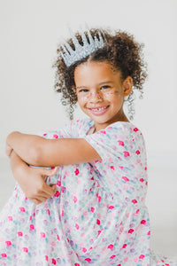 Girl wearing Mermaid Scales Short Sleeve Pocket Twirl Dress for Girls, silver crown and glitter freckles, smiling.
