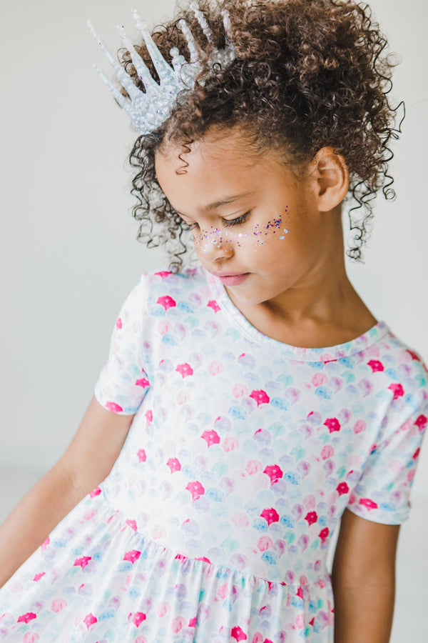 Girl wearing Mermaid Scales Short Sleeve Pocket Twirl Dress; pastel scale print, full twirl skirt, crown headband.