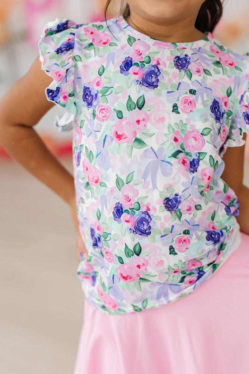 Adorable girl showcasing the Lavender Love S/S Ruffle Tee, featuring a vibrant floral design perfect for playful adventures, paired with a cute skirt.