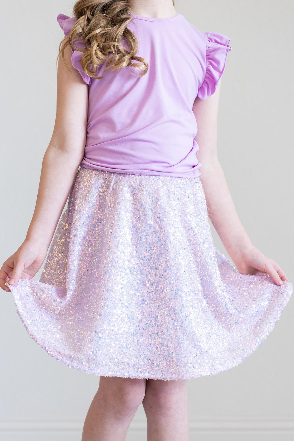 A young girl displaying the Lavender Sequin Twirl Skort by Mila & Rose, featuring dazzling lavender sequins that sparkle as she twirls. Perfect for any special occasion!