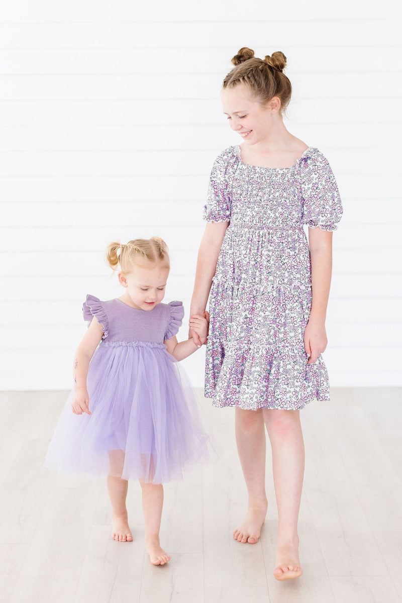 Two girls showcasing the Lovely Lavender Smocked Ruffle Dress, igniting a whimsical vibe with their playful poses.