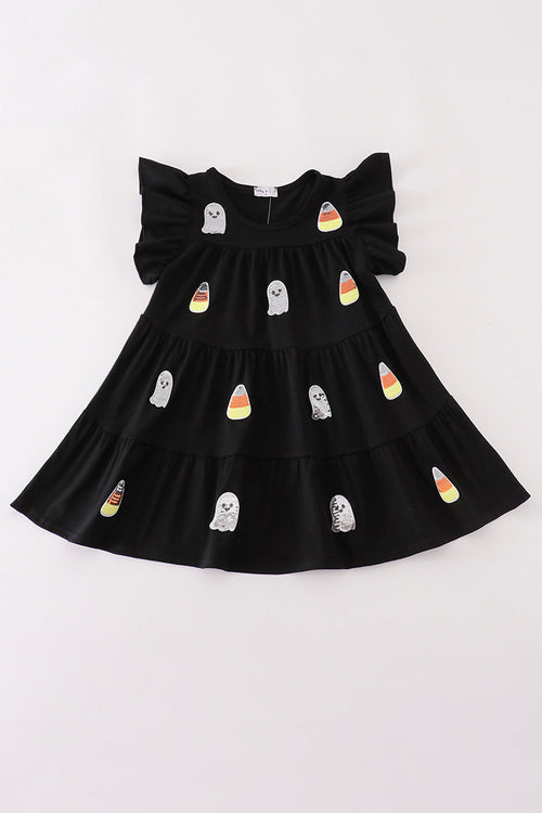 A black tiered baby dress with ruffled shoulder straps, decorated with cute ghost and candy corn illustrations, laid flat on a white background.