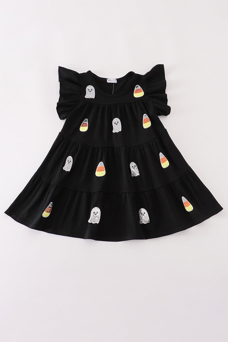 A black tiered baby dress with ruffled shoulder straps, decorated with cute ghost and candy corn illustrations, laid flat on a white background.