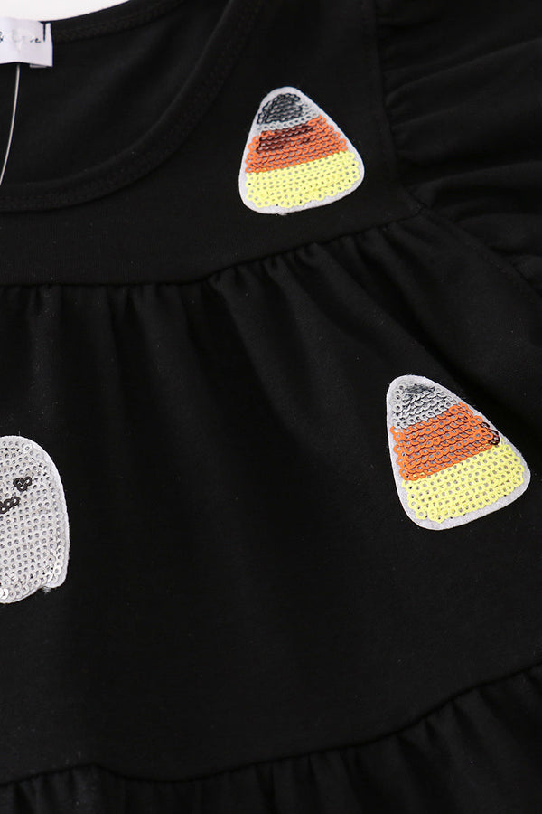 Close-up of a black ruffled garment featuring two sequined candy corn patches and part of a white sequined ghost patch on the front.