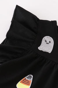 Close-up of a black ruffled garment with a ghost-shaped rhinestone patch and a candy corn patch on a white background.