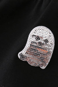 A ghost-shaped sequin patch with a white border, featuring black and silver sequins for a face and orange sequins for the body, displayed on a black fabric background.