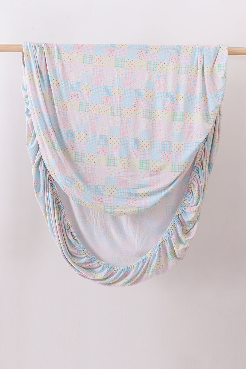 Pink floral checkered bamboo crib sheet with pastel patchwork pattern and elastic corners for soft, breathable baby bedding.