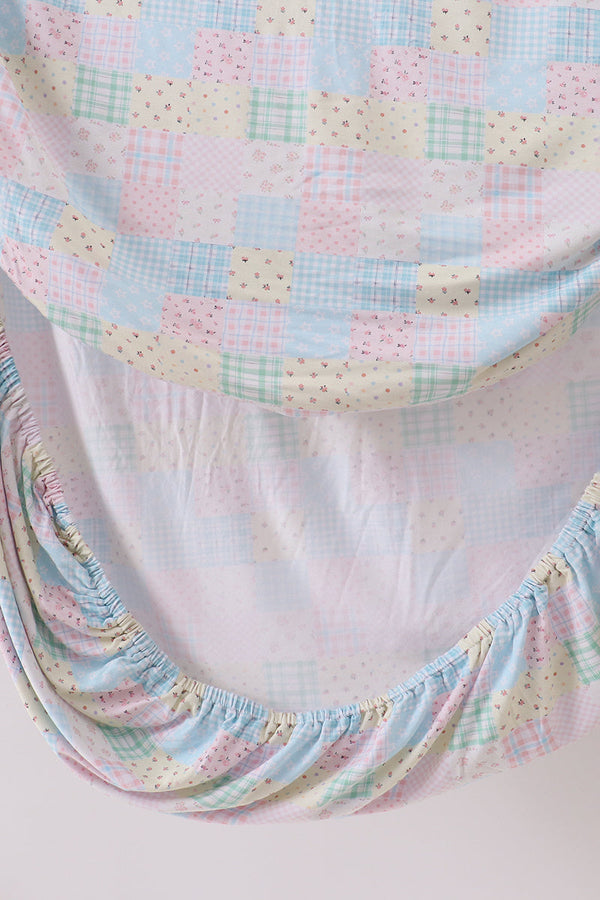 Pink floral patchwork crib sheet featuring a soft checkered pattern in pastel shades with elasticized edges for a secure fit.