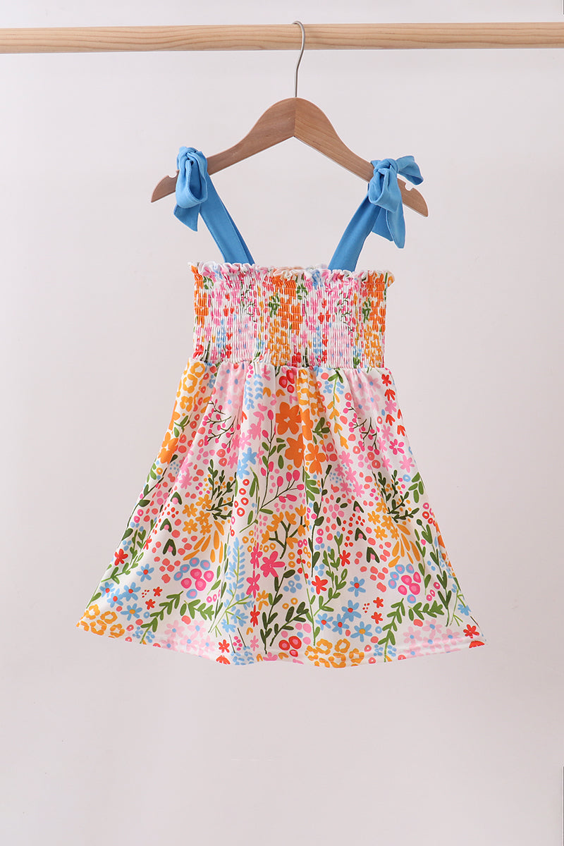 Colorful floral dress with blue straps on a hanger against a plain background