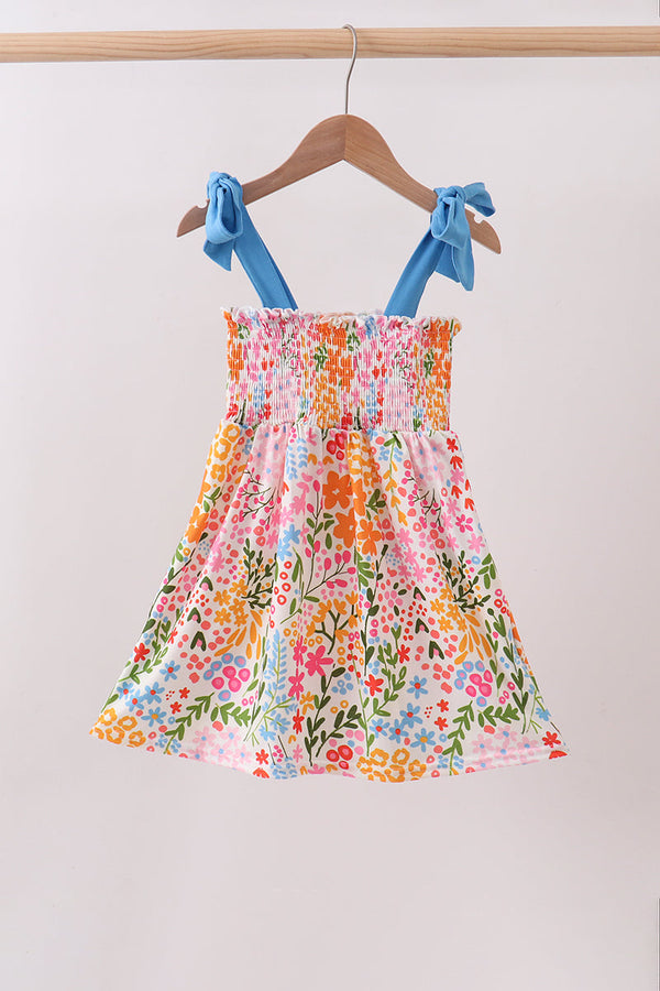Colorful floral dress with blue straps on a hanger against a plain background
