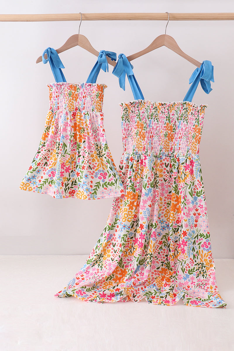 Floral dress with blue ribbon straps hanging on a rack against a white background
