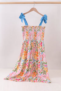 Floral dress with blue ribbon straps on a hanger against a white background