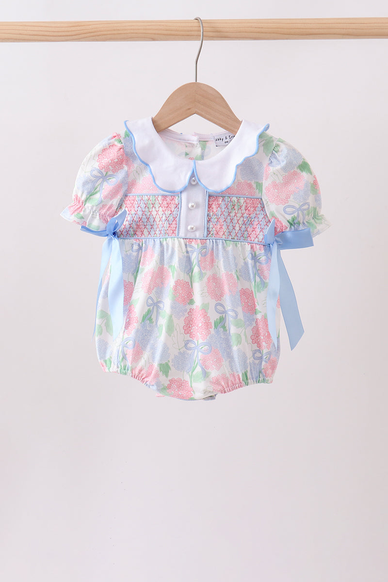 Floral baby romper with a white collar on a wooden hanger against a white background