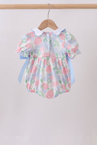 Floral baby romper with ruffled collar and sleeves on a wooden hanger against a white background
