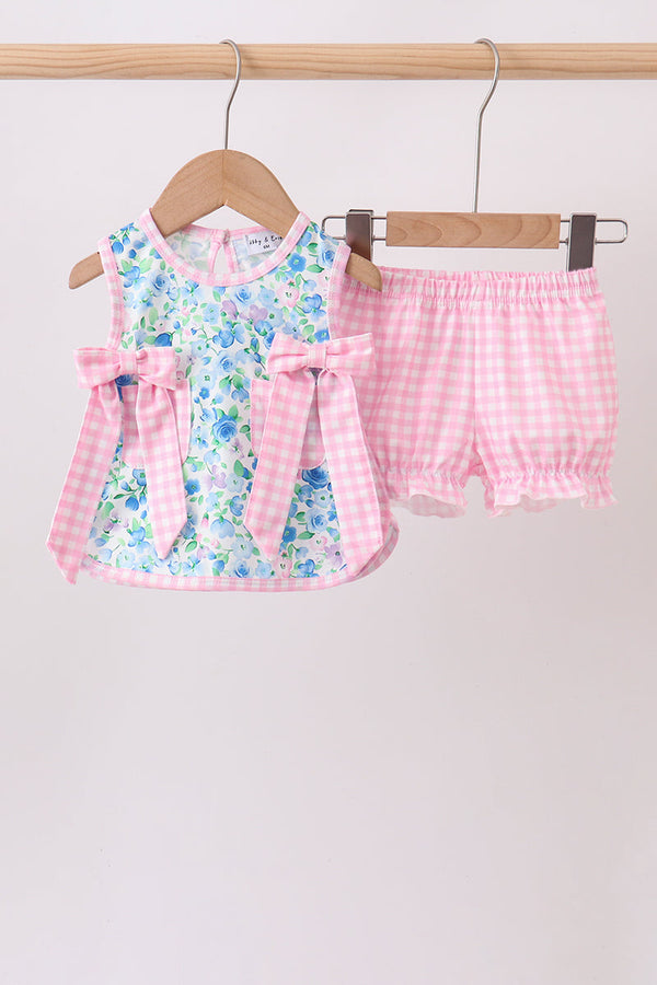 Blue floral top with pink gingham bows paired with pink checkered ruffle bloomers hanging on a wooden hanger.