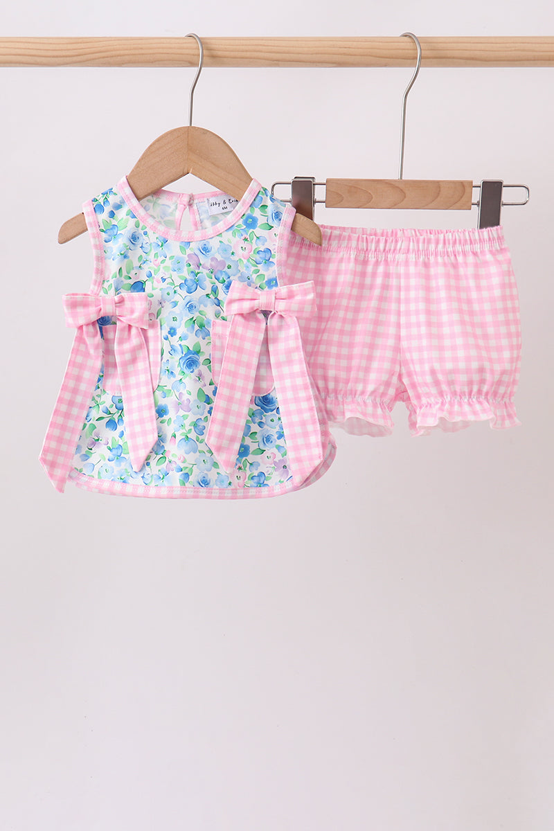 Blue floral top with pink gingham bows paired with pink checkered ruffle bloomers hanging on a wooden hanger.