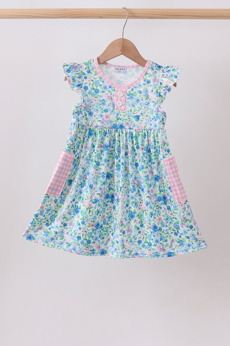 Blue floral dress with pink gingham pockets and flutter sleeves hanging on a wooden hanger.