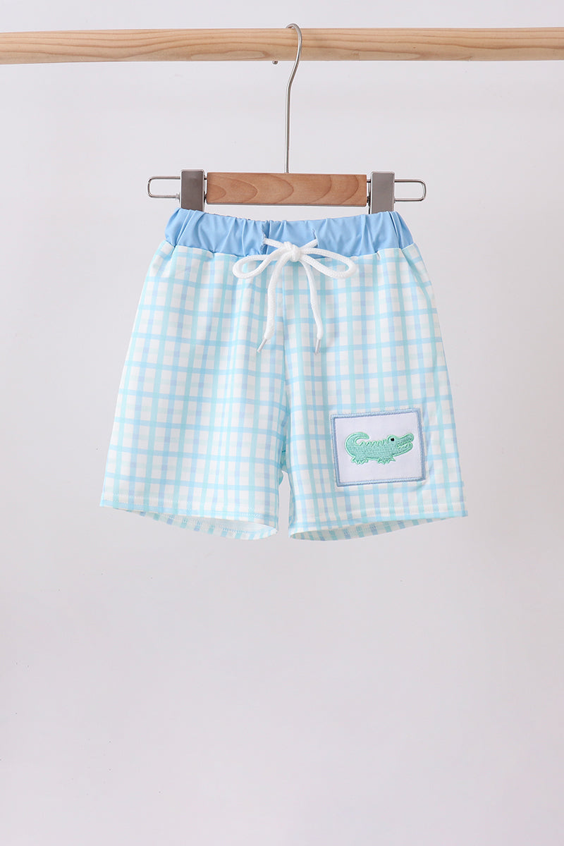 Blue crocodile-embroidered swim trunks with light blue gingham fabric and a drawstring waist.