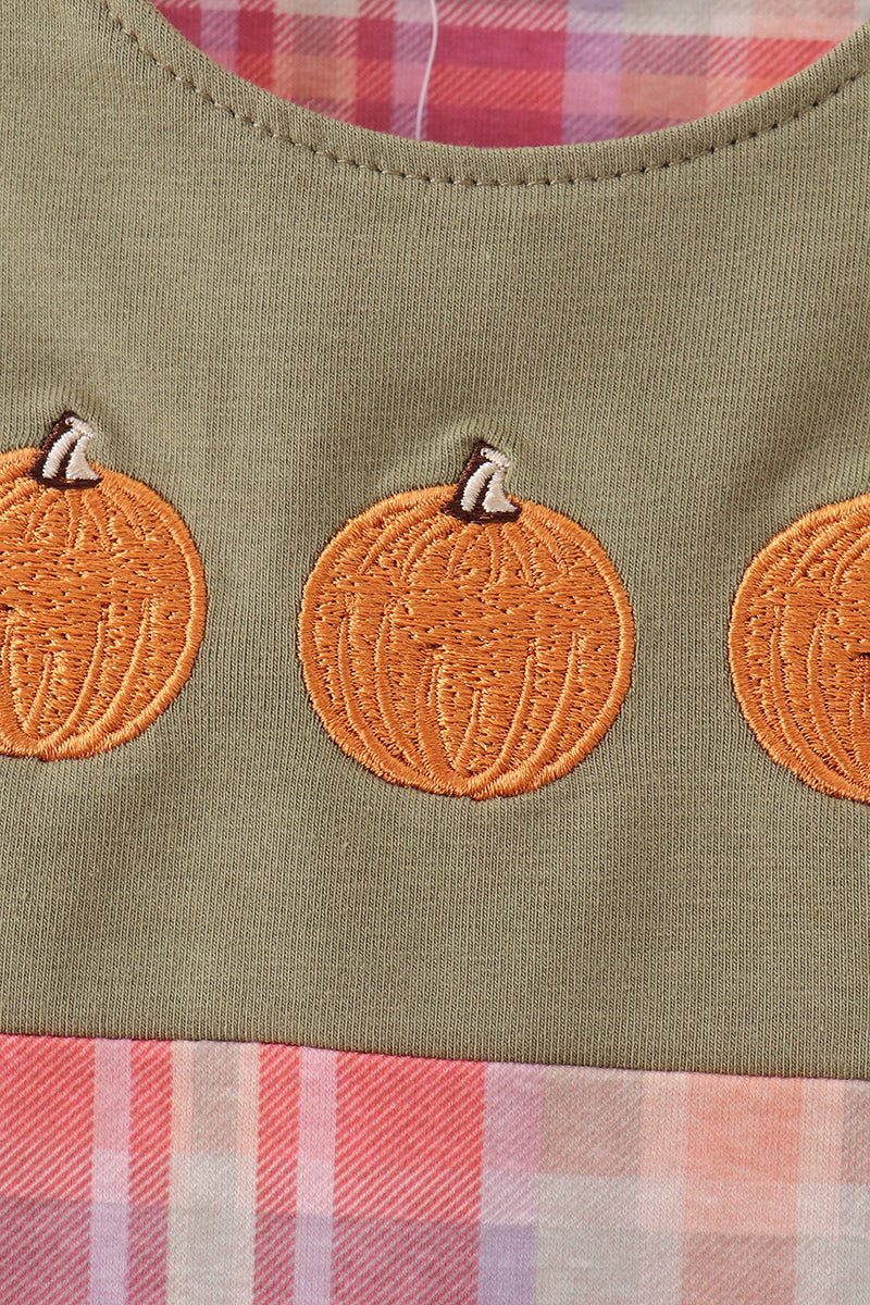 Close-up of a garment featuring orange pumpkin appliques on an olive green fabric, with a pink and white plaid lining visible at the neckline and bottom edge.
