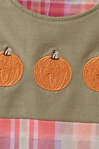 Close-up of a garment featuring orange pumpkin appliques on an olive green fabric, with a pink and white plaid lining visible at the neckline and bottom edge.