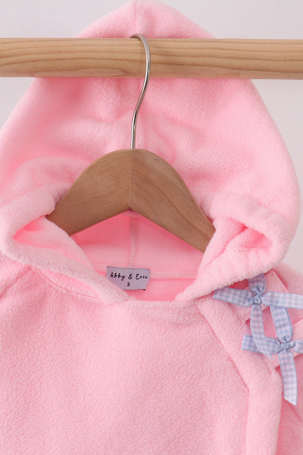 A close-up of a pink hooded baby garment hanging on a wooden hanger, with a small light blue gingham bow detail on the side and a visible Abby & Eve brand label.