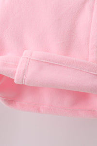 Close-up of a soft pink fleece or plush fabric with folded edges and a stitched hem, shown against a very light neutral background.