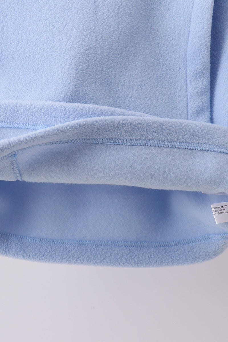 Close-up of plush light blue fleece coat hem showing soft texture, durable stitching, and tag for toddler comfort.