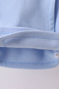 Close-up of plush light blue fleece coat hem showing soft texture, durable stitching, and tag for toddler comfort.