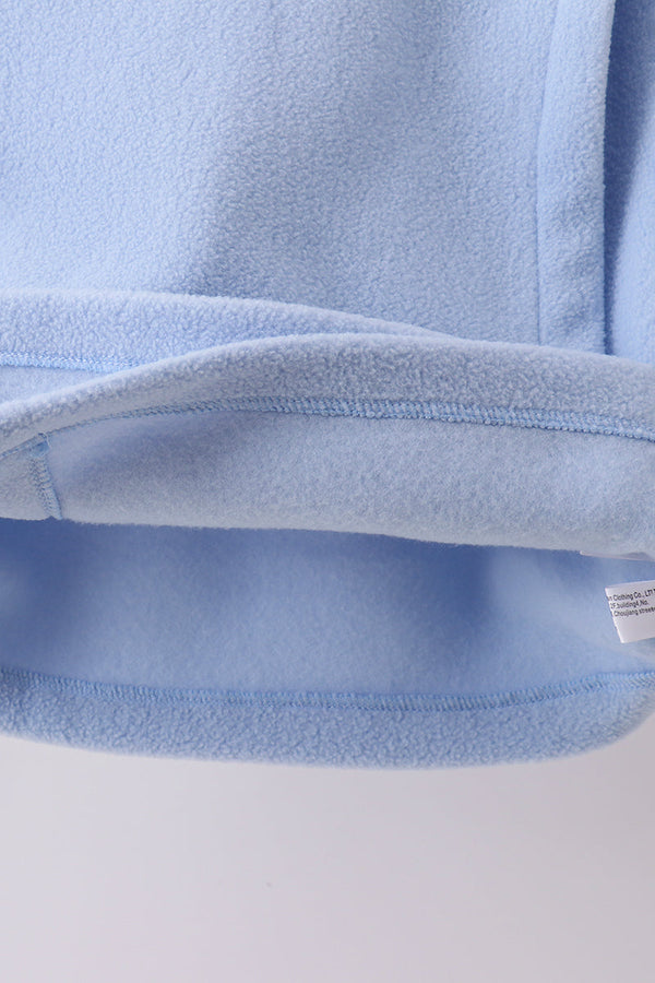 Close-up of plush light blue fleece coat hem showing soft texture, durable stitching, and tag for toddler comfort.