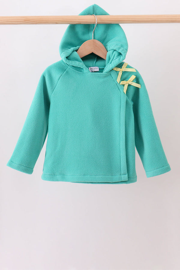 A turquoise long-sleeve hooded sweatshirt hanging on a wooden hanger from a wooden clothes rack, featuring yellow ribbon accents on the shoulder.