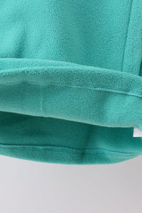 Close-up of a teal fleece fabric product, showing the soft textured material and folded edges against a light gray background.