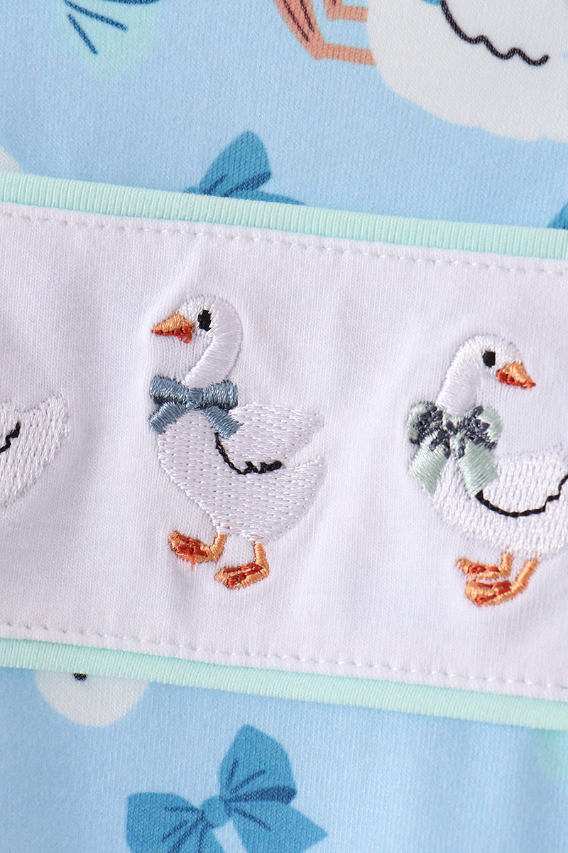 White goose embroidery with bow details on ruffled trim of a soft blue baby romper.