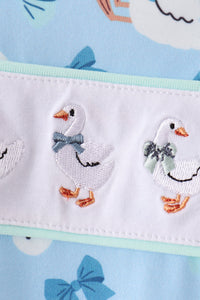 White goose embroidery with bow details on ruffled trim of a soft blue baby romper.