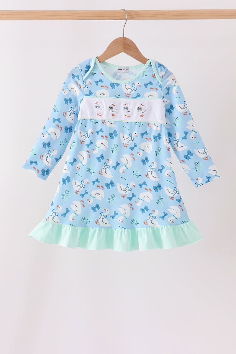 Blue children's dress with goose print, bow details, white chest panel, and mint green ruffle hem hanging on a wooden hanger.