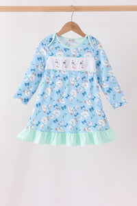 Blue children's dress with goose print, bow details, white chest panel, and mint green ruffle hem hanging on a wooden hanger.