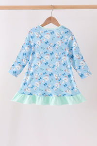 Back view of blue goose print dress with bow pattern and mint green ruffle hem hanging on a wooden hanger.
