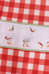 Red gingham fabric featuring embroidered white geese with party hats on a white band with green trim.