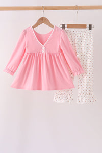 Pink girls set with long-sleeve V-neck top featuring white pom pom trim and white polka dot pants with ruffled legs.